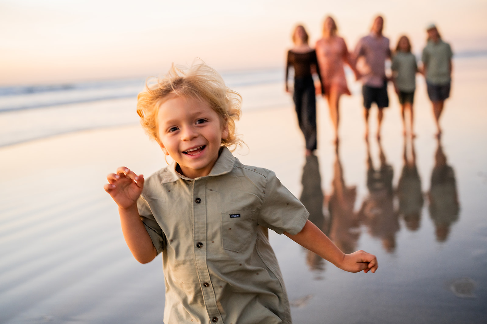 A boy running on the beach at sunset with his family walking behind him