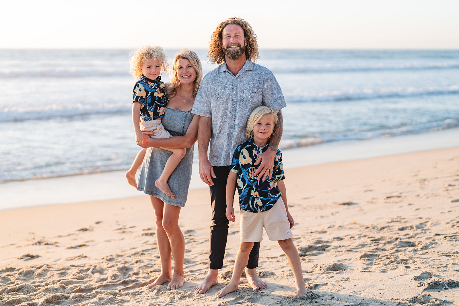 Family in coordinated tropical prints and neutrals, barefoot on the beach